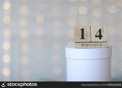 Valentine&rsquo;s day concept. Date 14 February on wooden cube calendar on a white gift box and white heart in hand. Bokeh golden and white background.. Valentine&rsquo;s day concept. Date 14 February on wooden cube calendar on a white gift box and white heart in hand. Bokeh golden and white background