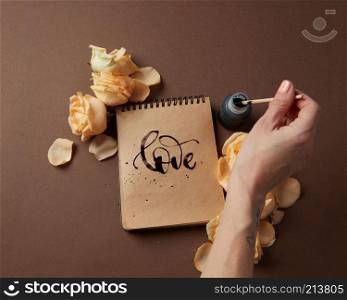 Valentine&rsquo;s Day concept. Diary or notebook with word love written by female. Female&rsquo;s hand writing in diary with brown pages over brown background.. Diary or notebook with word love