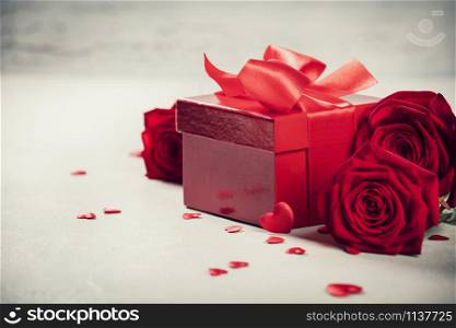 Valentine&rsquo;s Day concept. Gift with red bow on the wooden background Valentines gift box tied with a red satin ribbon bow on rustic background.. Valentine&rsquo;s Day concept. Valentines gift boxes tied with a red satin ribbon bow and beautiful roses on rustic background.