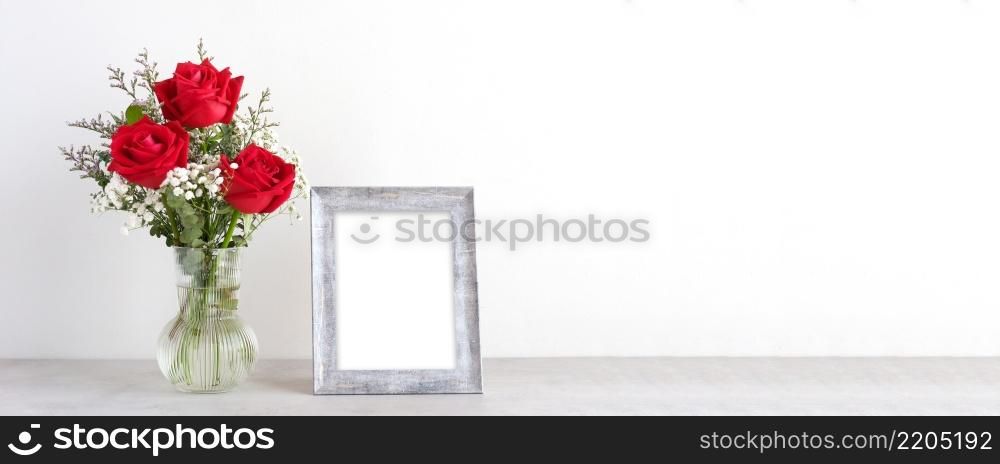 Valentine&rsquo;s day concept, Red roses flower bouquet in glass vase and blank grey vintage wooden frame on table background with copy space , Banner for mock up, template