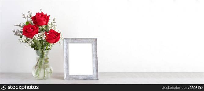 Valentine&rsquo;s day concept, Red roses flower bouquet in glass vase and blank grey vintage wooden frame on table background with copy space , Banner for mock up, template