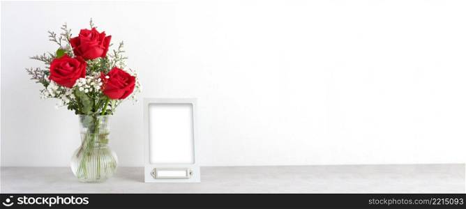Valentine&rsquo;s day concept, Red roses flower bouquet in glass vase and blank grey vintage frame on table background with copy space , Banner for mock up, template