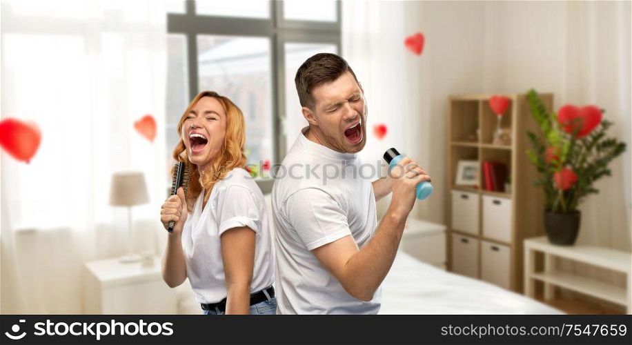 valentine&rsquo;s day, fun and people concept - portrait of happy couple in white t-shirts couple singing to hairbrush and lotion bottle over home bedroom decorated with heart shaped balloons background. couple singing to hairbrush and lotion at home