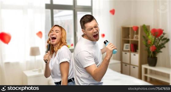 valentine&rsquo;s day, fun and people concept - portrait of happy couple in white t-shirts couple singing to hairbrush and lotion bottle over home bedroom decorated with heart shaped balloons background. couple singing to hairbrush and lotion at home