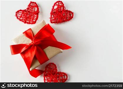 Valentine&rsquo;s day gift and red hearts on a white background. Holiday background for Valentine&rsquo;s day - a gift with a red satin ribbon and handmade hearts on a white background, photo for design.. Valentine&rsquo;s day gift and red hearts on a white background