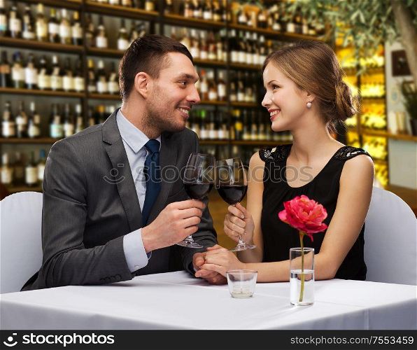 valentine&rsquo;s day, leisure and luxury concept - smiling couple clinking glasses of red wine over restaurant background. happy couple drinking red wine at restaurant