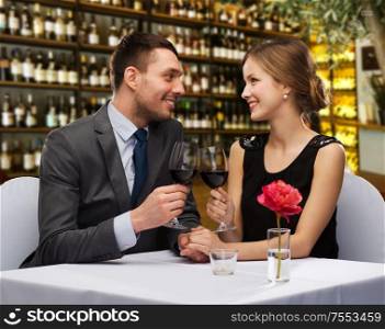 valentine&rsquo;s day, leisure and luxury concept - smiling couple clinking glasses of red wine over restaurant background. happy couple drinking red wine at restaurant