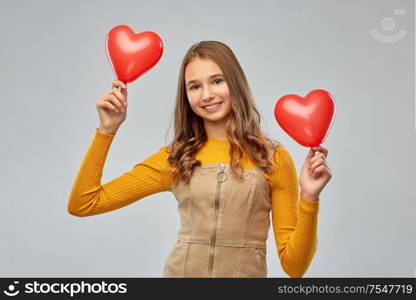 valentine&rsquo;s day, love and people concept - smiling young teenage girl with red heart-shaped balloons over grey background. happy teenage girl with red heart-shaped balloons