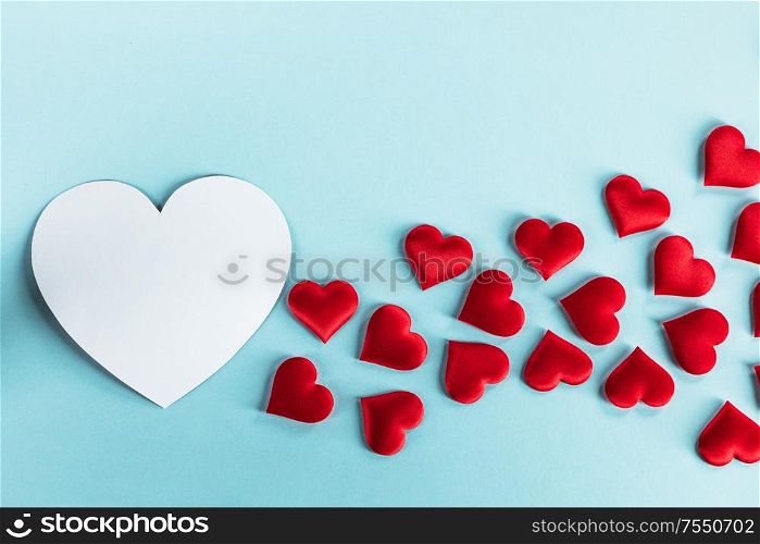 Valentine&rsquo;s day many red silk hearts and white heart shape card on blue paper background , border frame on red with copy space, love concept. Valentines day hearts on blue