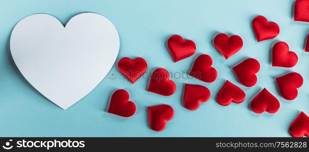 Valentine&rsquo;s day many red silk hearts and white heart shape card on blue paper background , border frame on red with copy space, love concept. Valentines day hearts on blue