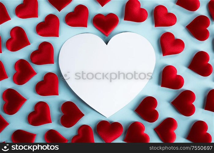 Valentine&rsquo;s day many red silk hearts and white heart shaped card on blue background, love concept. Valentines day hearts on blue