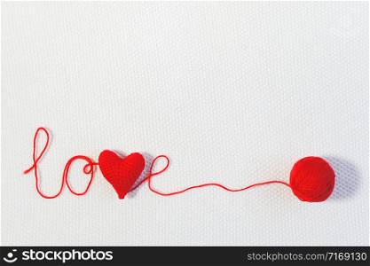 Valentine&rsquo;s day or wedding backdrop. Red knitted volume heart in the word love and ball of thread on white knitted background. Template for design, valentines card, invitation. Copy space Top view.. Valentine&rsquo;s day or wedding backdrop. Red knitted volume heart in the word love and ball of thread on white knitted background. Template for design, valentines card, invitation. Copy space Top view