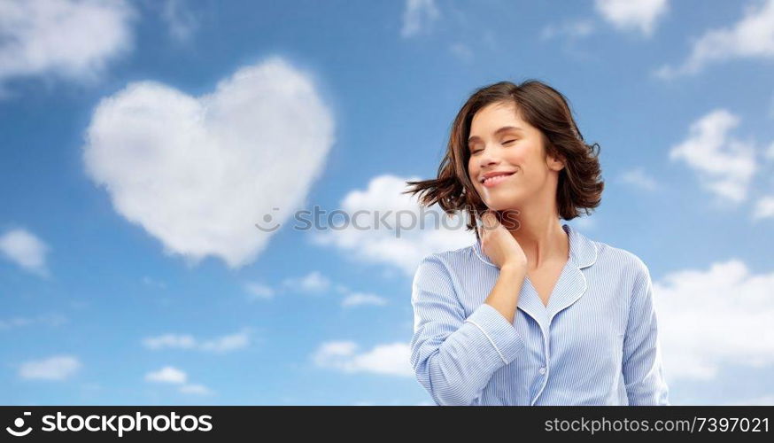 valentine&rsquo;s day, people and bedtime concept - happy young woman in pajama whipping her hair over background. happy young woman in pajama over sky background