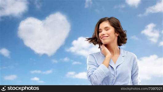 valentine&rsquo;s day, people and bedtime concept - happy young woman in pajama whipping her hair over background. happy young woman in pajama over sky background