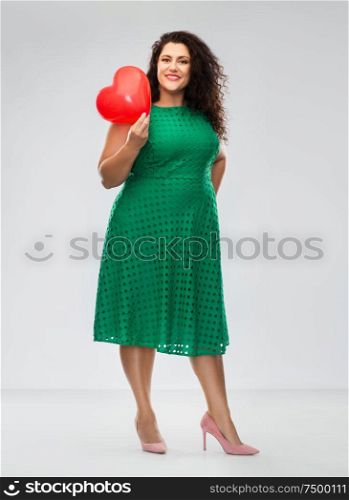 valentine&rsquo;s day, people and love concept - happy woman in green dress holding red heart shaped balloon over grey background. happy woman holding red heart shaped balloon