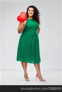 valentine&rsquo;s day, people and love concept - happy woman in green dress holding red heart shaped balloon over grey background. happy woman holding red heart shaped balloon