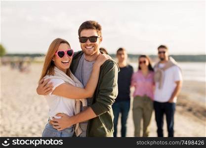 valentine&rsquo;s day, relationships and people concept - happy couple with group of friends hugging on beach in summer. happy friends walking along summer beach
