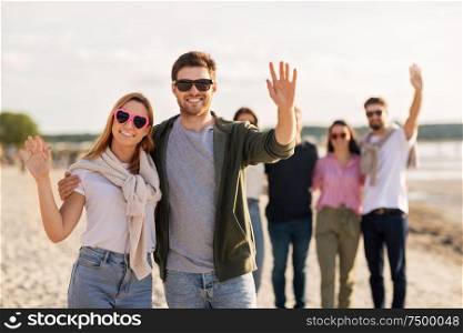 valentine&rsquo;s day, relationships and people concept - happy couple with group of friends on beach in summer waving hands. happy couple with friends waving hands on beach