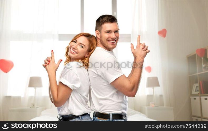 valentine&rsquo;s day, relationships and people concept - portrait of happy couple in white t-shirts making gun gesture over bedroom decorated with heart shaped balloons background. happy couple making gun gesture on valentines day
