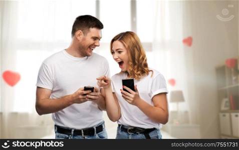 valentine&rsquo;s day, technology and people concept - happy couple in white t-shirts with smartphones over home bedroom decorated with heart shaped balloons background. happy couple in white t-shirts with smartphones