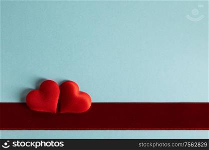 Valentine&rsquo;s day two red silk hearts and red satin ribbon on blue paper background, love concept. Valentines day hearts on blue