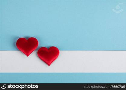 Valentine&rsquo;s day two red silk hearts and white paper on blue paper background, love concept. Valentines day hearts on blue