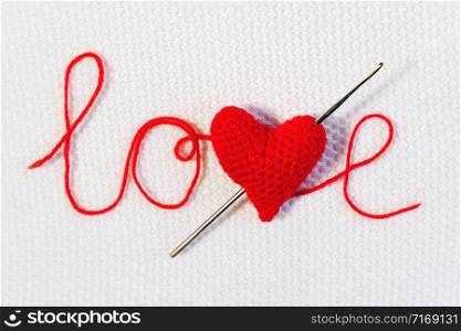 Valentine&rsquo;s day, wedding backdrop. Crochet hook pierced red knitted volume heart like an arrow in word love from threads on white knitted background. Template for design, valentines card, invitation.. Valentine&rsquo;s day, wedding backdrop. Crochet hook pierced red knitted volume heart like an arrow in word love from threads on white knitted background. Template for design, valentines card, invitation