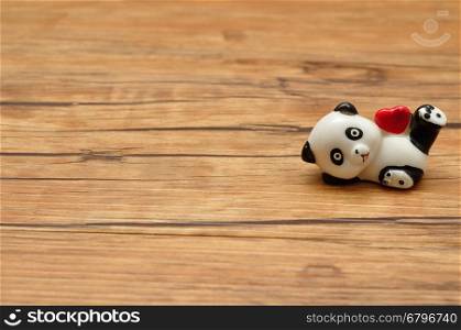 Valentine's Day. A ceramic panda figurine holding a red heart isolated against a wooden background