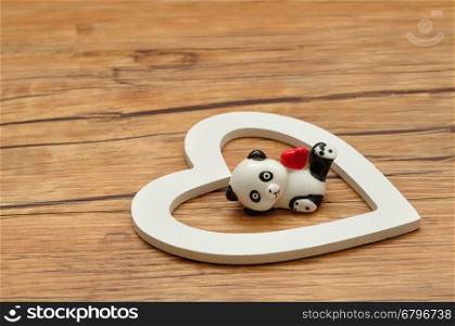 Valentine's Day. A ceramic panda figurine with a red heart inside a white wooden heart
