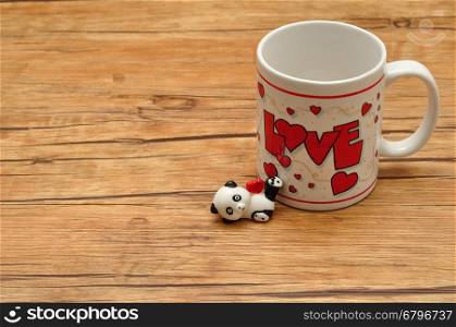 Valentine's Day. A white mug with the word love on it with a ceramic panda figurine holding a red heart