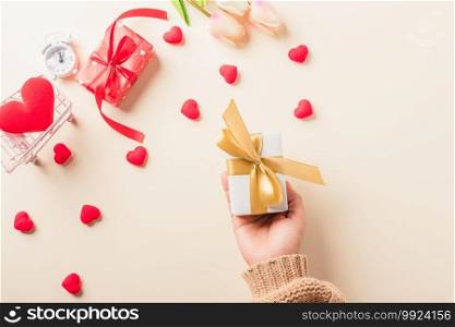 Valentine’s day and birthday. Woman hands holding gift or present box decorated and red heart surprise on cream pastel background, Female’s hand hold gift box package in craft paper Top view flat lay