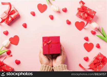 Valentine’s day and birthday. Woman hands holding gift or present box decorated and red heart surprise on pink background, Female’s hand hold gift box package in craft paper Top view flat lay