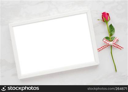 Valentine?s day background, template, Red rose and blank white wooden frame on white marble background with copy space for text, flat lay