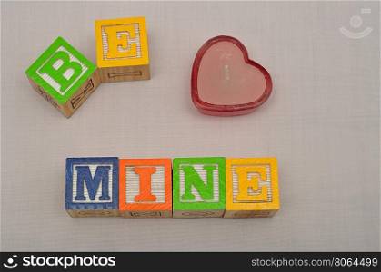 Valentine's Day. Be Mine Spelled with colorful alphabet blocks and a red heart shape candle