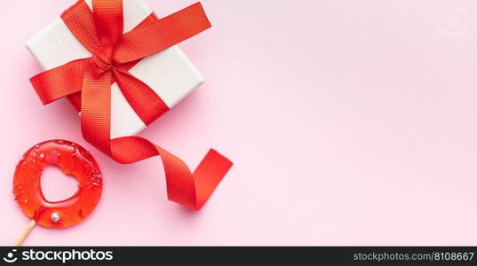 Valentine’s Day concept. Top view photo of gift box, heart shaped lollipop on pastel pink background with copy space in the middle. 