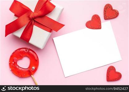 Valentine’s Day concept. Top view photo of gift box, heart shaped lollipop on pastel pink background with copy space in the middle. 