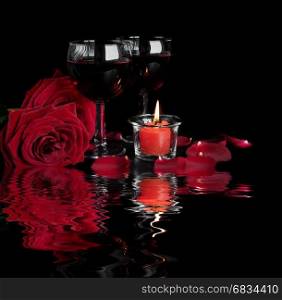 Valentine's Days concept: two glasses of red wine, two red roses and a burning red candle isolated on a black background reflected in a water surface with small waves
