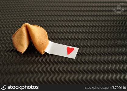 Valentines day. A fortune cookie with a piece of paper with a red heart displayed on a black background