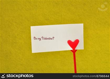 Valentines day. A note holder with a red heart with a note reading be my valentine isolated against a yellow background