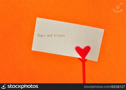 Valentines day. A note holder with a red heart with a note reading hugs and kisses isolated against an orange background
