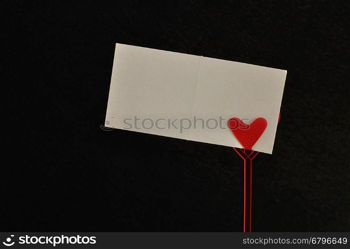 Valentines day. A note holder with a red heart with an empty card isolated against a black background