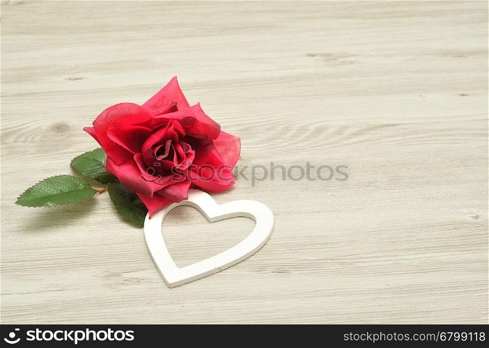 Valentines day. A white heart with an artificial red rose isolated against a wooden background
