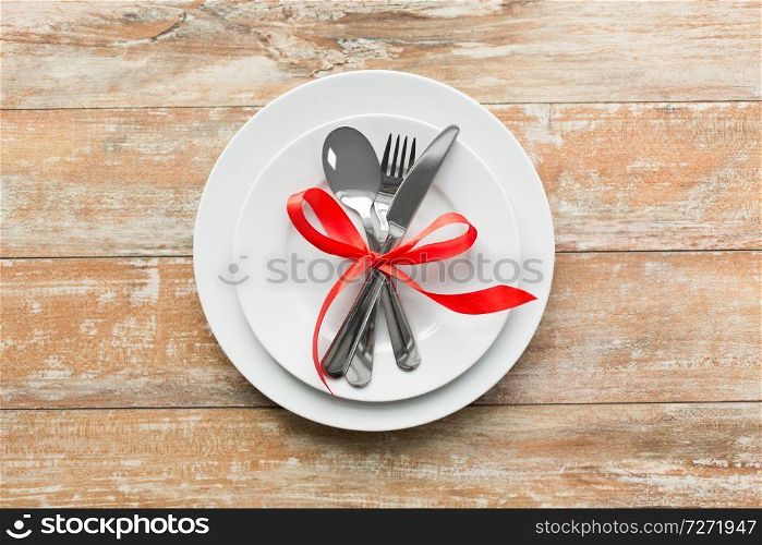 valentines day and festive dinner concept - plate with spoon, knife and fork tied with red ribbon on wooden table from top. cutlery tied with red ribbon on set of plates
