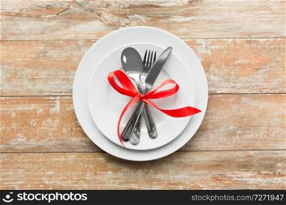 valentines day and festive dinner concept - plate with spoon, knife and fork tied with red ribbon on wooden table from top. cutlery tied with red ribbon on set of plates