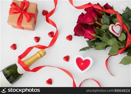 valentines day and holidays concept - close up of champagne, gift, red heart shaped chocolate candies, candle and red roses. close up of champagne, gift, candies and red roses