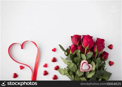 valentines day and holidays concept - close up of red roses and heart shaped chocolate candies on white background. close up of red roses and heart shaped candies