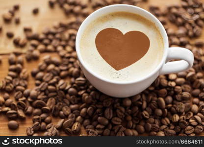 valentines day and hot drinks concept - close up coffee cup with heart stencil picture and roasted beans on wooden table. coffee cup with heart and roasted beans