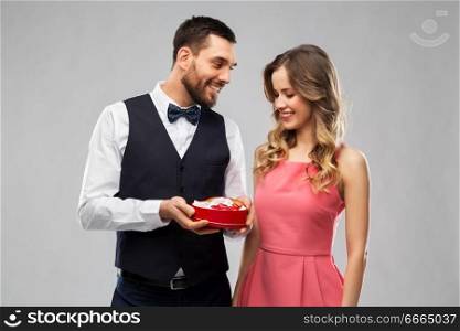 valentines day and people concept - happy couple with chocolate box in shape of heart over grey background. happy couple with chocolate box in shape of heart