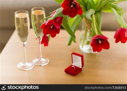 valentines day and romantic concept - diamond ring in red velvet gift box, champagne glasses and flowers on table. diamond ring, champagne and flowers on table