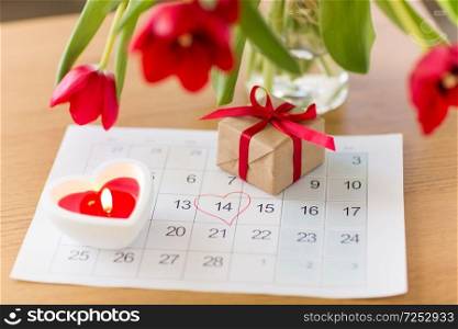 valentines day and romantic concept - gift box, calendar sheet with 14th february date marked by heart shape and flowers on table. gift box, calendar sheet and flowers on table